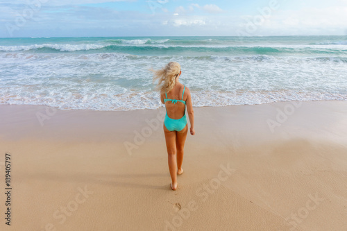 blonde girl in one piece turquoise swim suit going to swim to the stormy sea