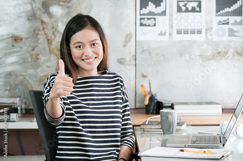 Canvas Print Young asian businesswoman thump up and smiling while sitting at her desk office,