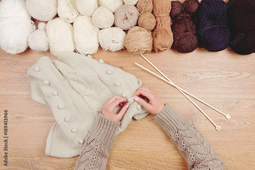 Dressmaker workplace. Woman female girl hands knitting warm sweater by knitted needles on wooden background with line of balls of thread