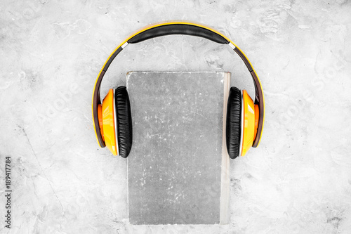 Listen audiobook concept. Headphones on a book on grey background top view