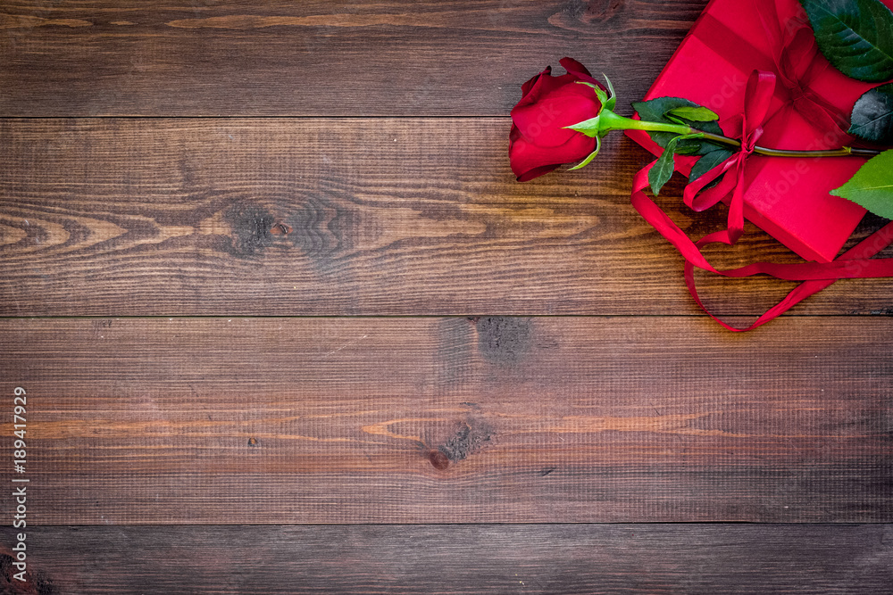 Prepare the prsesnts or surprise for Valentine's day. Red gift box near red rose on dark wooden background top view space for text Prepare the prsesnts or surprise for Valentine's day. Red gift box near red rose on dark wooden background top view space for text
