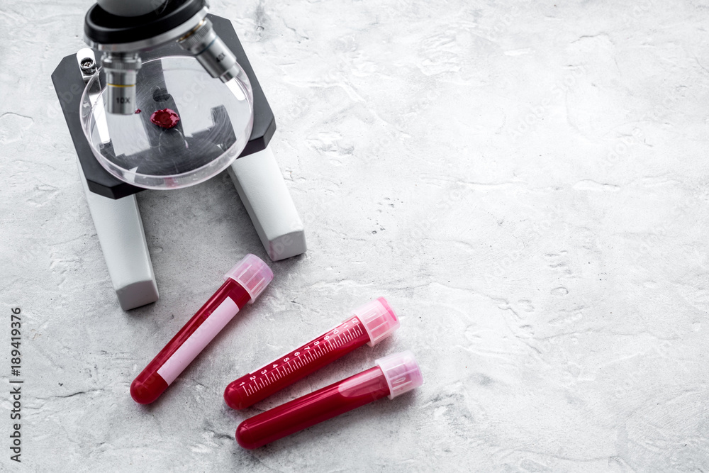 Blood analysis in clinacal lab. Test tubes near microscope on grey background top view copy space Blood analysis in clinacal lab. Test tubes near microscope on grey background top view copy space