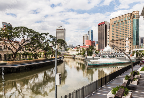 Canvas Print The office and the  Sultan Abdul Samad buildings reflect in the water of the Klang river in front of the Jamek mosque (masjid) in the heart of Kuala Lumpur in Malaysia