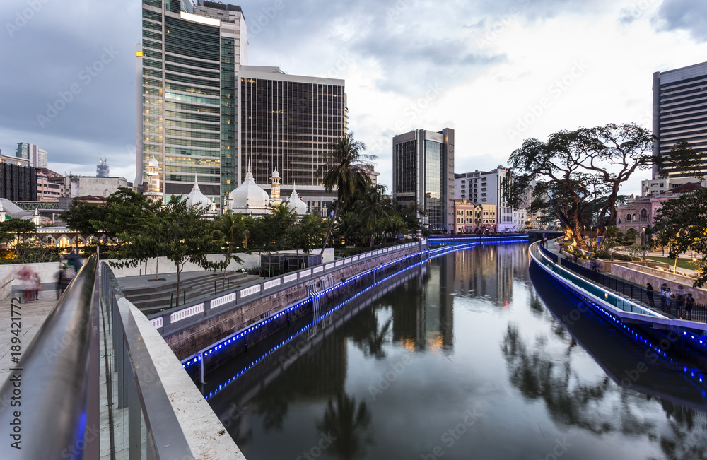 Obraz premium The office buildings reflects in the water of the Klang river in front of the Jamek mosque in the heart of Kuala Lumpur in Malaysia.