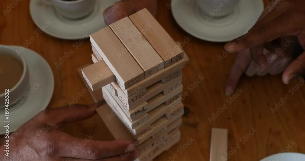 Friends playing jenga game on table while having coffee in bar 