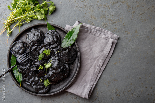 Traditional Italian black ravioli on black plate, gray stone slate background. Top view