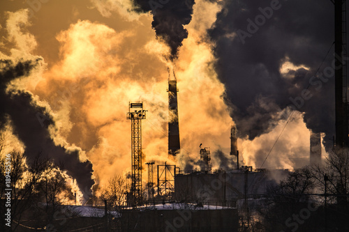 the chimneys of a refinery with smoke and steam with the pinkk sunset on the background