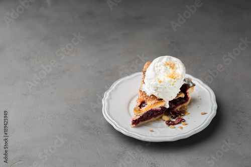 A piece of cherry pie with vanilla ice cream on a white vintage plate on a gray light concrete background. Copy Space. View blank space for text.