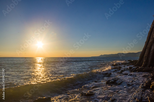 Amazing sea sunset on the pebble beach, the sun, waves, clouds