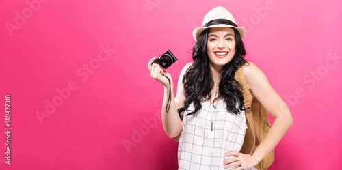 Traveling young woman holding a camera on a solid background