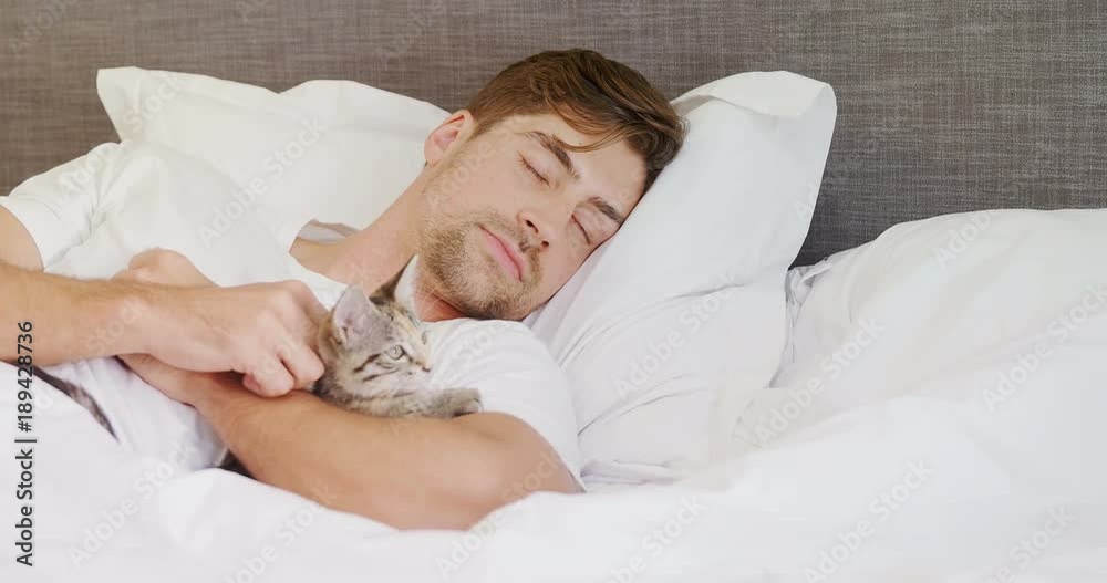 Young man sleeping on bed holding cat in his arms  