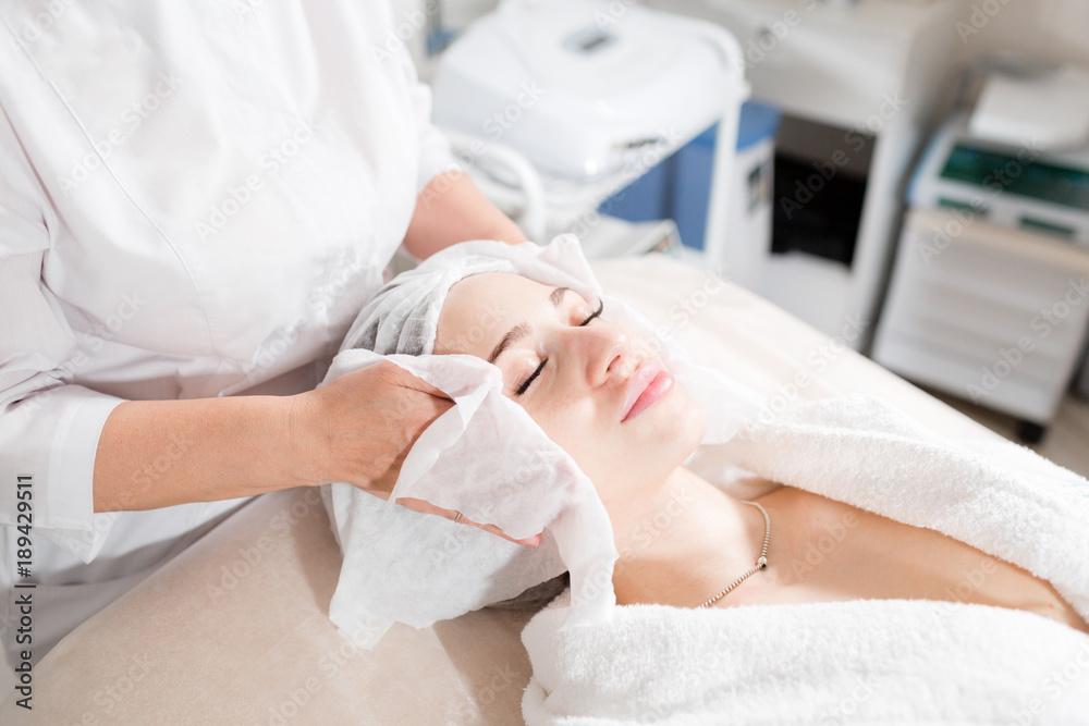 Fototapeta premium Wipe with sterile napkin face. Young pretty woman receiving treatments in beauty salons. Facial cleansing foam using.