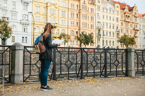A tourist with a backpack in front of a beautiful old architecture in Prague in the Czech Republic. She looks at the map.