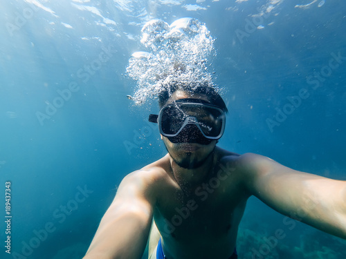 male diver swims in the sea under water with a mask and snorkel