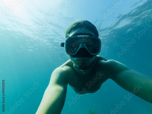 male diver swims in sea under water with a mask and snorkel