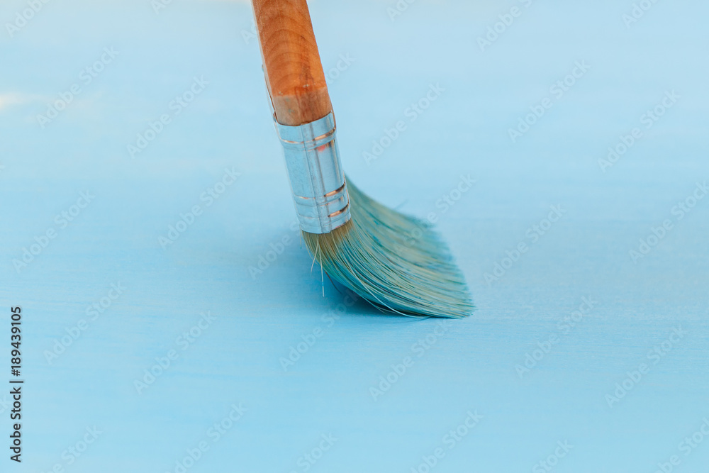 Staining the wooden surface with blue paint using a paint brush
