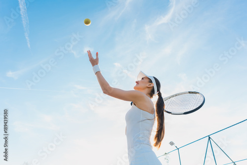 Woman playing tennis giving service throwing ball in the air