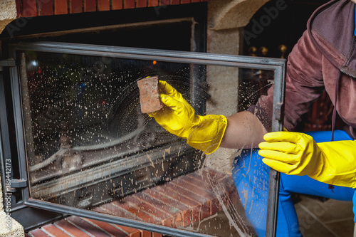 Hands in yellow gloves wash glass fireplace door