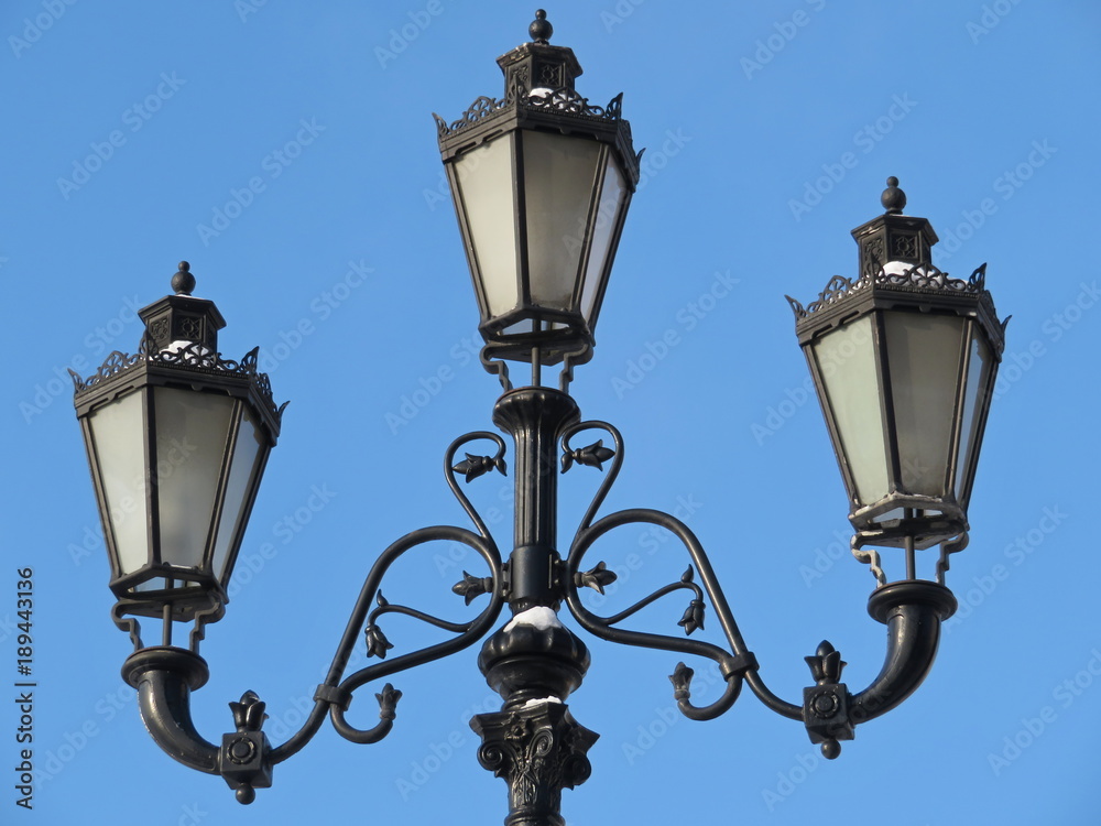 Street lamp on the background of blue sky. Snowy metal streetlight isolated