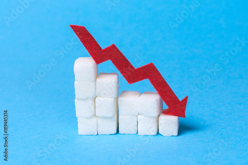 Reducing sugar content in the cow. Diabetes. Stairs of sugar cubes and a red arrow down on a blue background photo