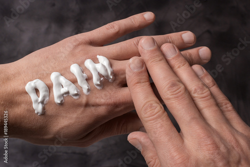 The word Pain is written in cream. Pain in the dry hands of a man in cream or ointment. Gray background