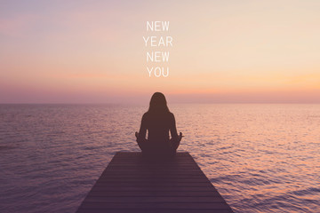 Inspirational quote " NEW YEAR NEW YOU"with woman meditating on a wooden bridge by the sea in the morning background with vintage filter.