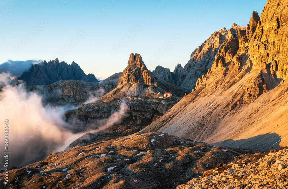 Dolomites Alps rocky mountain range and Rifugio Locatelli at sunset with cloud drift, Tre Cime di Lavaredo, Italy
