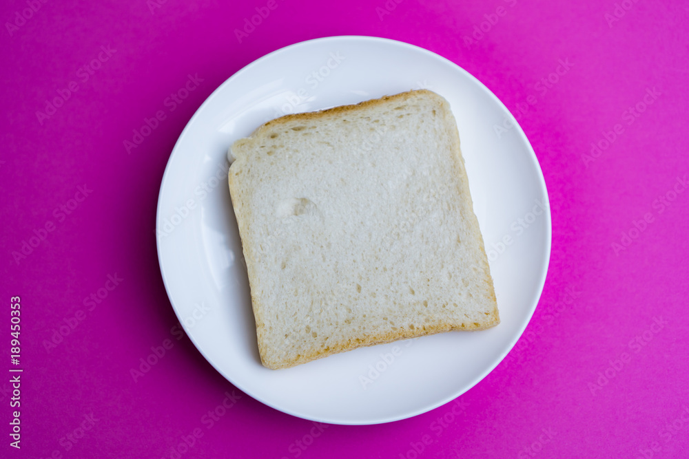 A slice of toast on a white plate, pink background