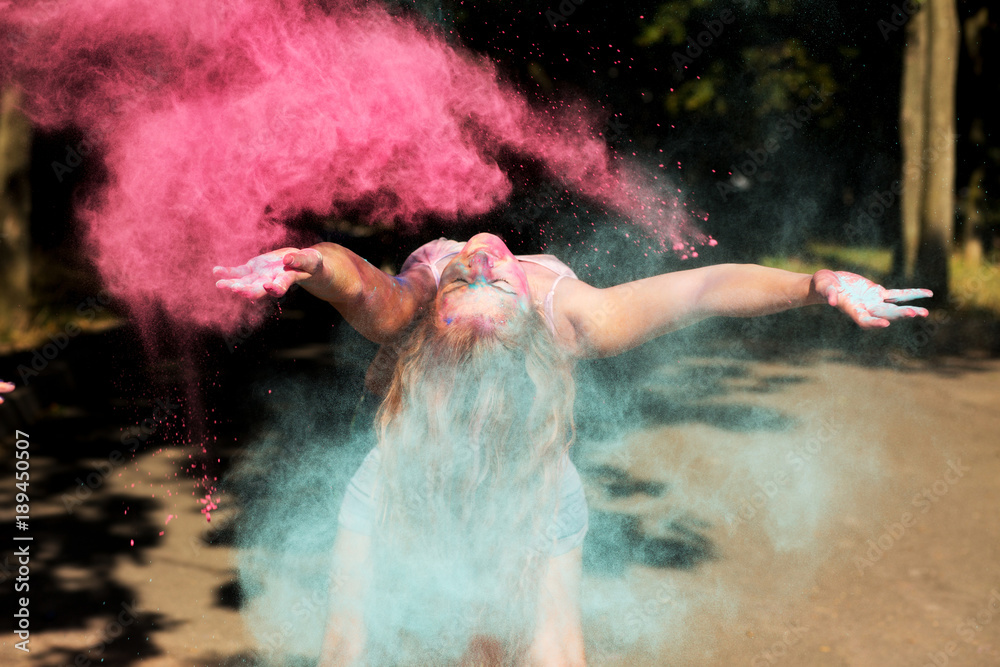 Cool young woman having fun with exploding dry Holi paint