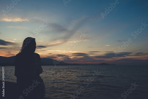 Silhouettes image of a woman looking at sea view on the beach with sunset background