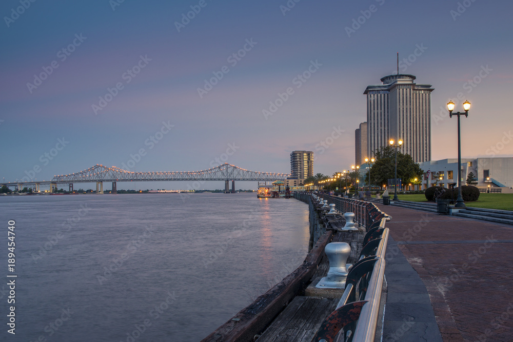 View of the Mississippi river from the city of New Orleans riverfront, with the Great New Orleans Bridge on the background in New Orleans, Louisiana, at dusk.