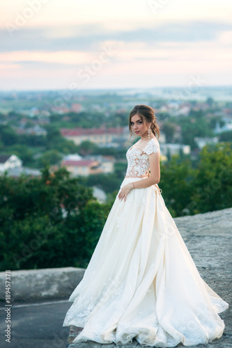 Young girl in wedding dress on city background at sunset. Summer