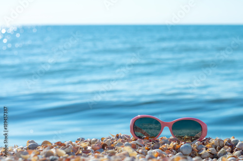 baby pink sun-glasses on the background of the sea horizon with the sun.