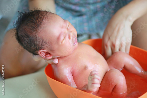 Close up hands of mother taking a bath to her newborn baby in a bathtub.