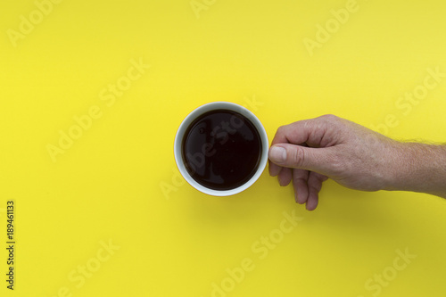 Hand holding coffee cup overhead on bright yellow background