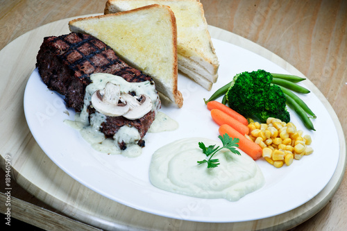 Roasted black pepper lamb steak with salads and fries on a blue round plate. Wooden texture background. photo