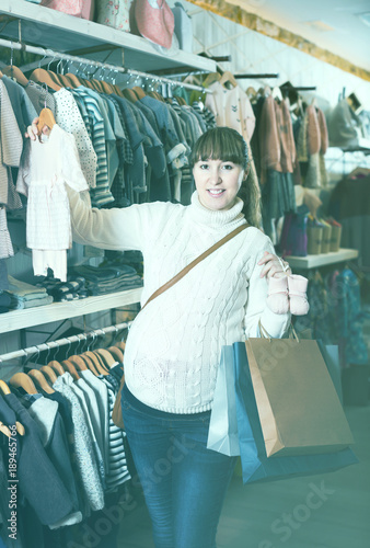 Happy pregnant woman choosing clothes for baby