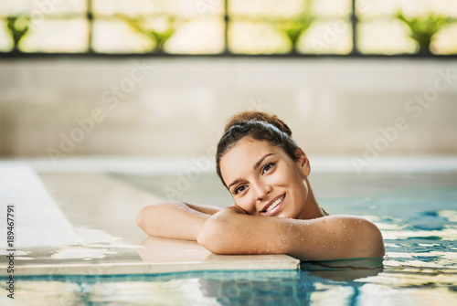 Young beautiful woman enjoying summer holiday in swimming pool at resort hotel. Spa, retreat, relaxation concept. Beauty, health and body care. Healthy living