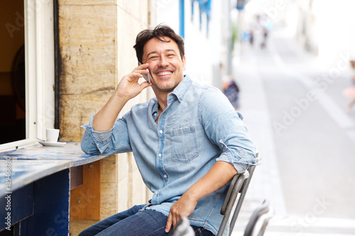 smiling mature man using mobile phone at street cafe