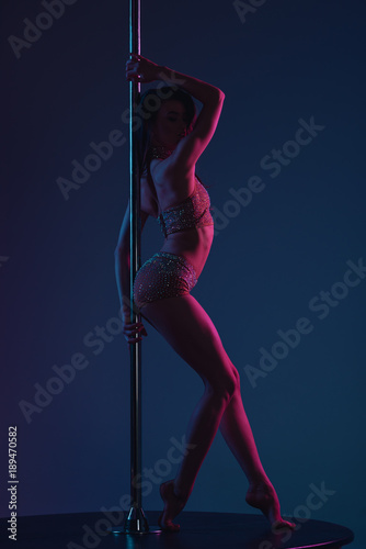 side view of beautiful sensual female dancer posing with pole on blue