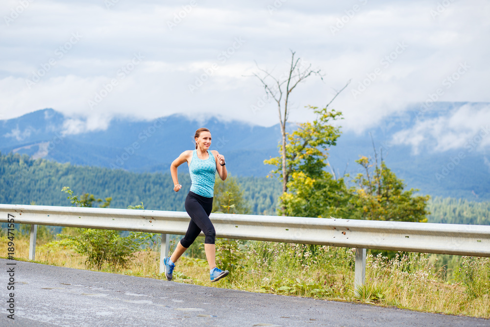 Young sporty woman jogging on mountain road. Running fitness girl in sportswear outdoor image with copy space