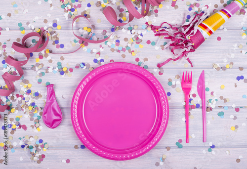 Celebratory wood background with confetti and balloons, with children plate, fork and knife in the middle. Copyspace Mockup ..