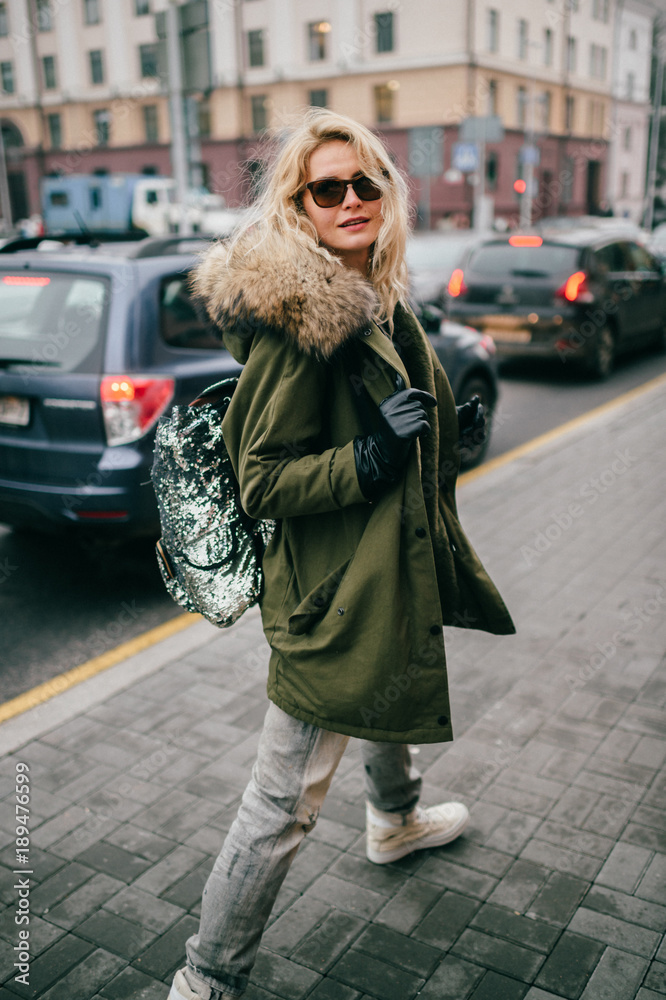Stylish fashionable blonde model girl walking in city street outdoor.  Expressive mood soft focus portrait of rebel youth teenager female in  trendy clothes and sunglasses. Cheerful happy cute woman. Stock Photo