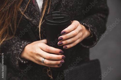 2637320 girl in stylish coat with beautiful manicure hand holding a black vacuum tumbler on a gray background