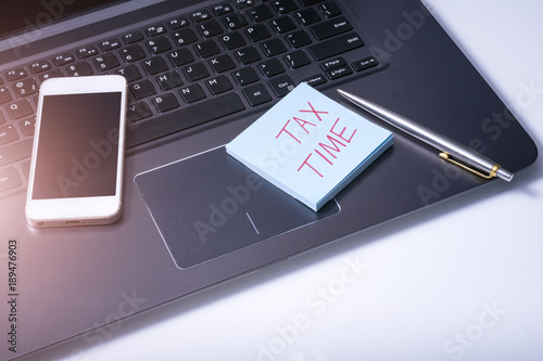 Sticker with words "TAX TIME" on computer notebook and pen. Business concept.