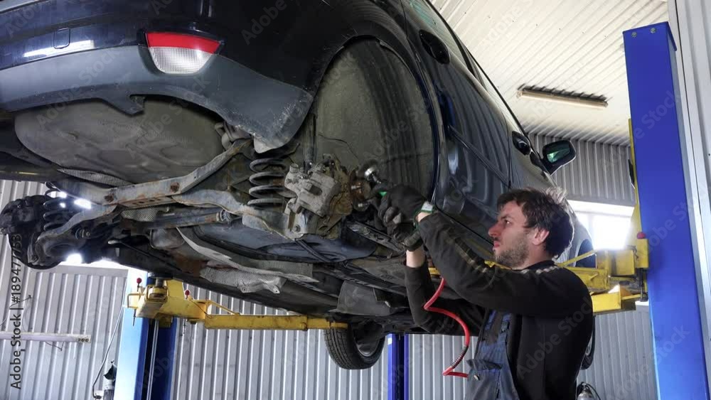 Mechanic worker man grind rusty bolts with electric grinder tool near lifted car