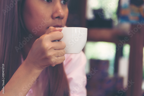 Be absent-minded women holds a white hot matcha green tea cup for drinking in the coffee shop. Middle age women drinking hot milk green tea while thinking about her work.