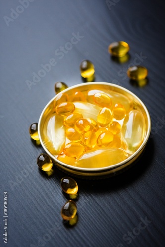 Capsules of fish oil in gold cup on black background