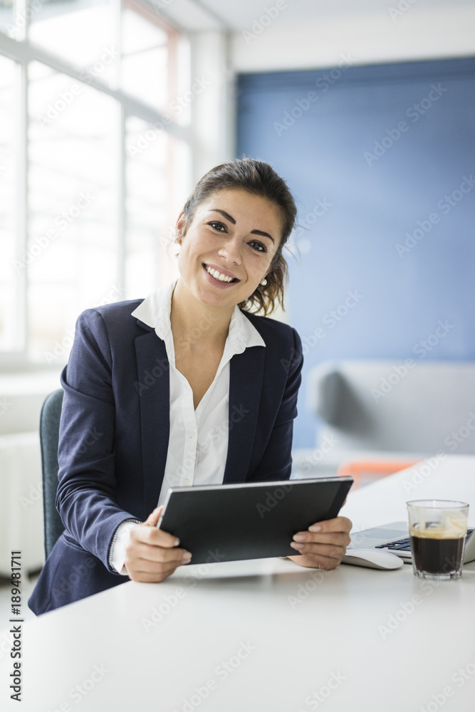 Portrait of happy businesswoman with tablet sitting at desk in the office Portrait of happy businesswoman with tablet sitting at desk in the office