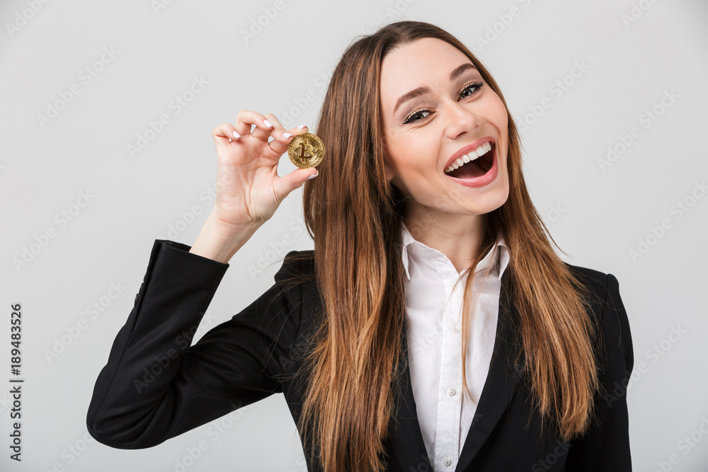Smiling pretty lady in suit looking camera and holding golden bitcoin isolated Smiling pretty lady in suit looking camera and holding golden bitcoin isolated